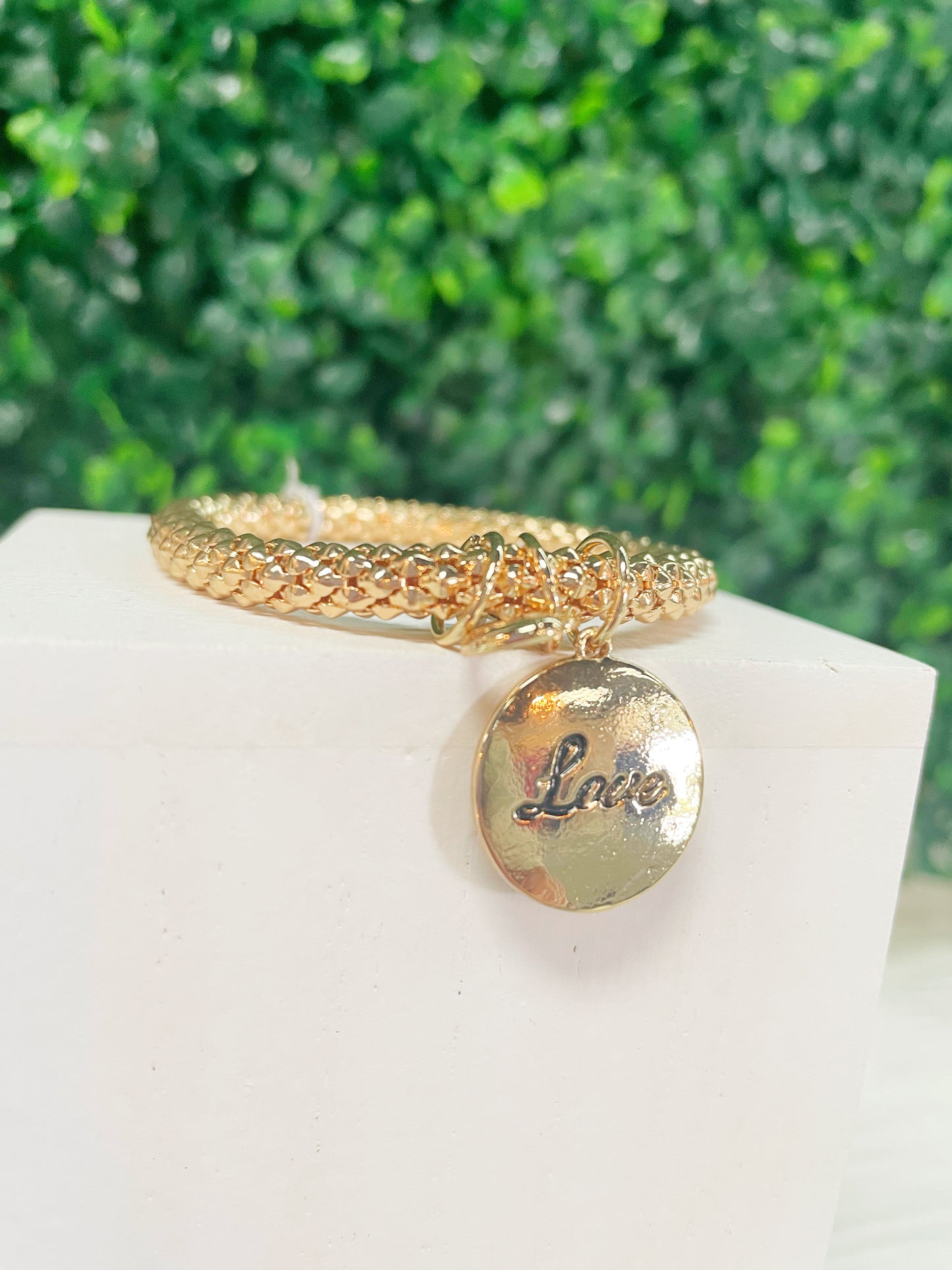 Gold bracelet with a gold charm that says "Love"