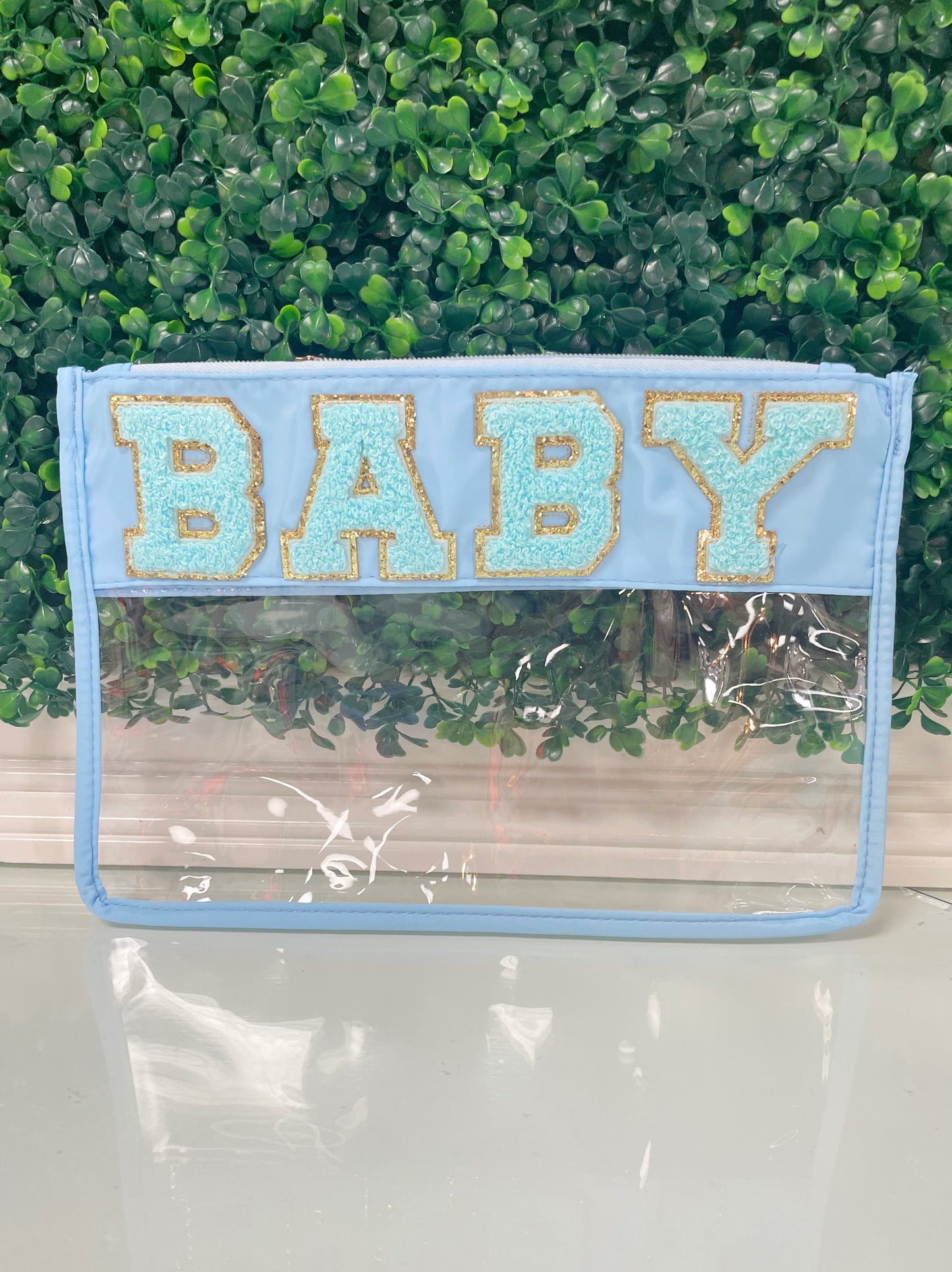 Clear zippered pouch that has a light blue border with the word 'baby' embroidered at the top in chenille light blue varsity letters outlined in shiny gold.