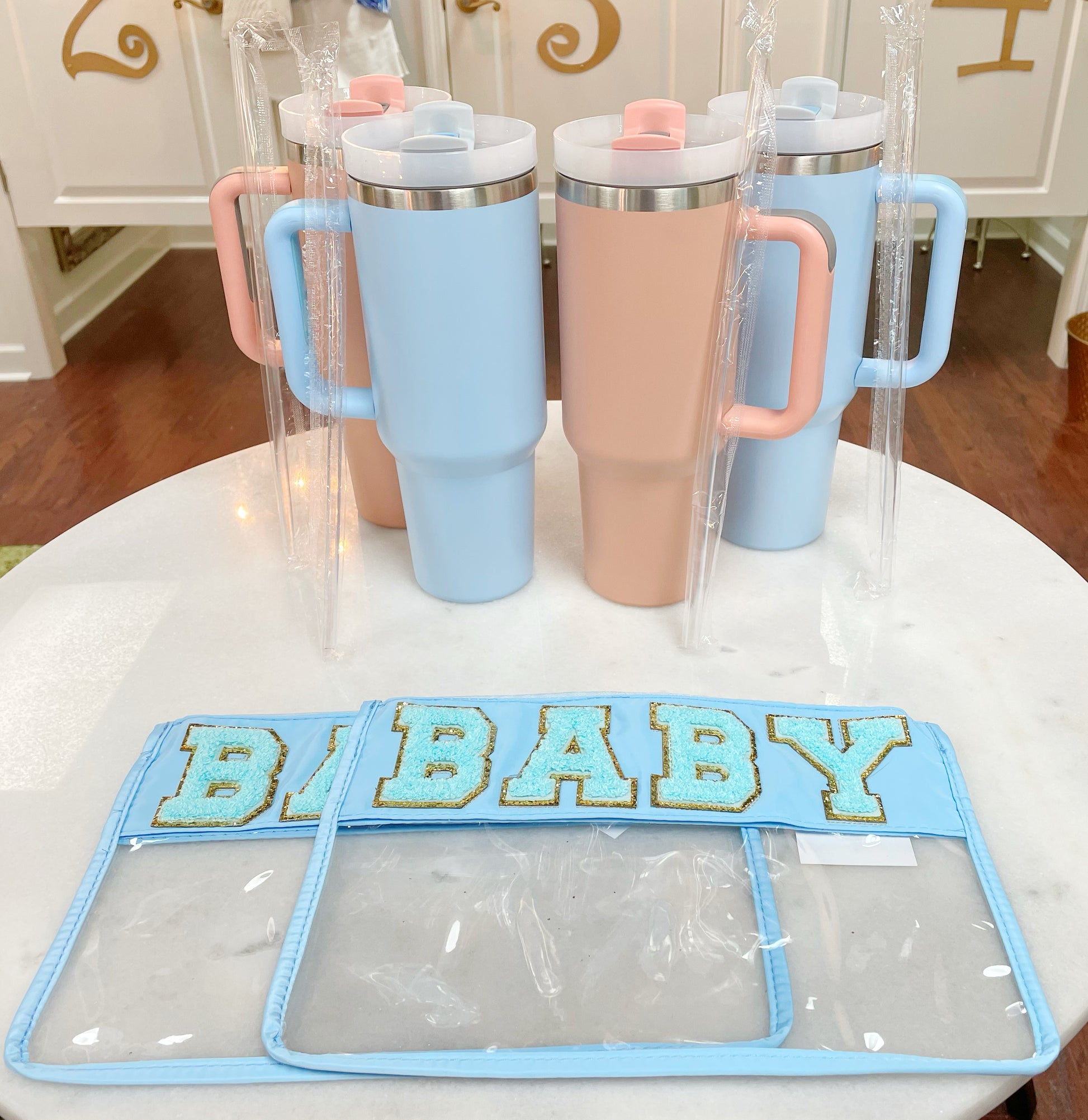 Clear zippered pouch that has a light blue border with the word 'baby' embroidered at the top in chenille light blue varsity letters outlined in shiny gold.