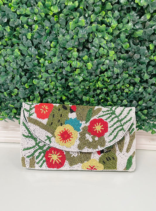 Vibrant, beaded clutch with an all-over floral design. The flowers and foliage showcase hues of red, yellow, blue, and green. Against a pristine white background, the intricate beadwork stands out, creating a visually captivating contrast.