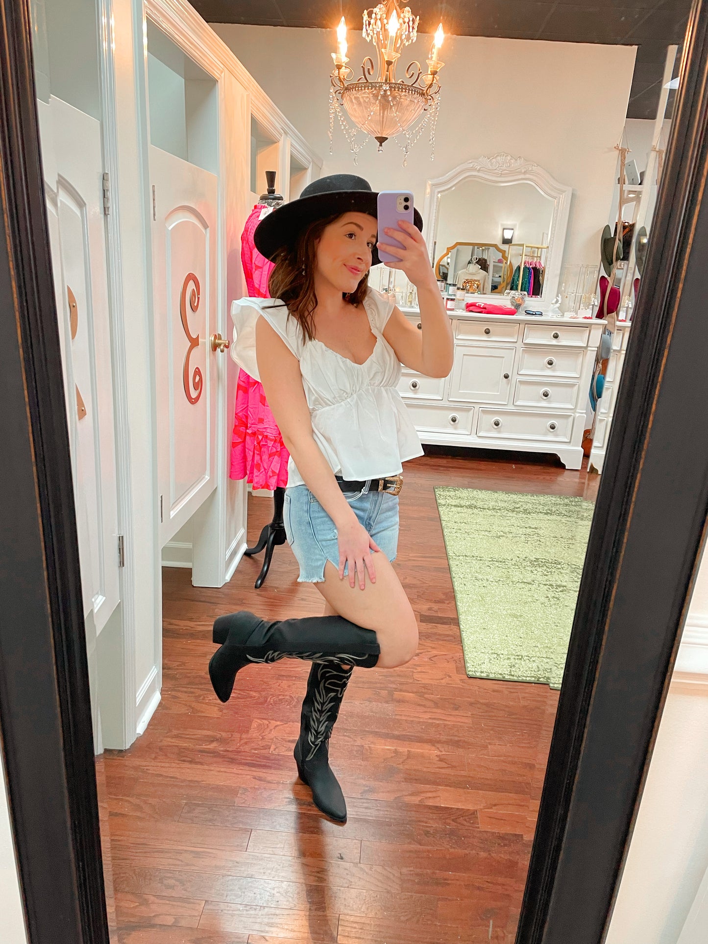 Tall black cowboy boots with embroidered detailing paired with light wash denim shorts, black wide brim fedora hat, and white blouse